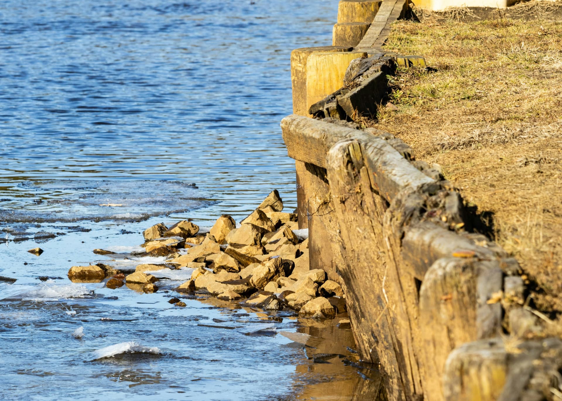 Damaged wooden bulkhead with separated cap boards and exposed riprap along the shoreline